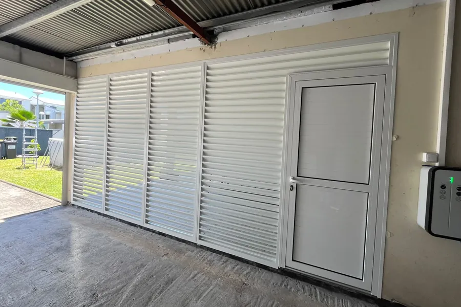 Brise-vue aluminium blanc à lames avec porte intégrée, fermant un carport