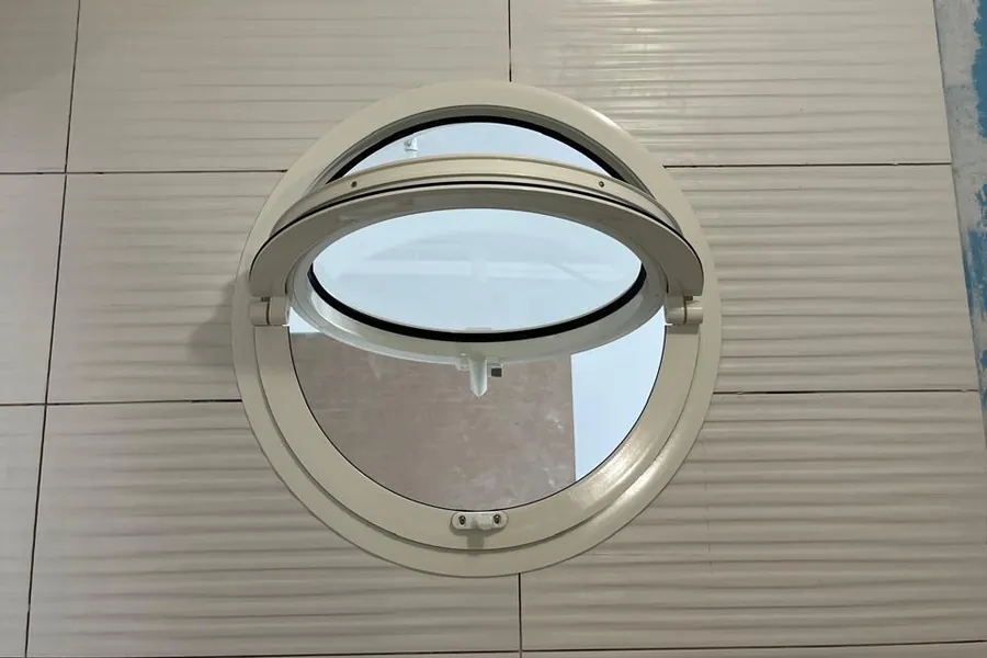 Œil-de-bœuf rond en aluminium, ouvrant à mi-hauteur, dans un mur carrelé