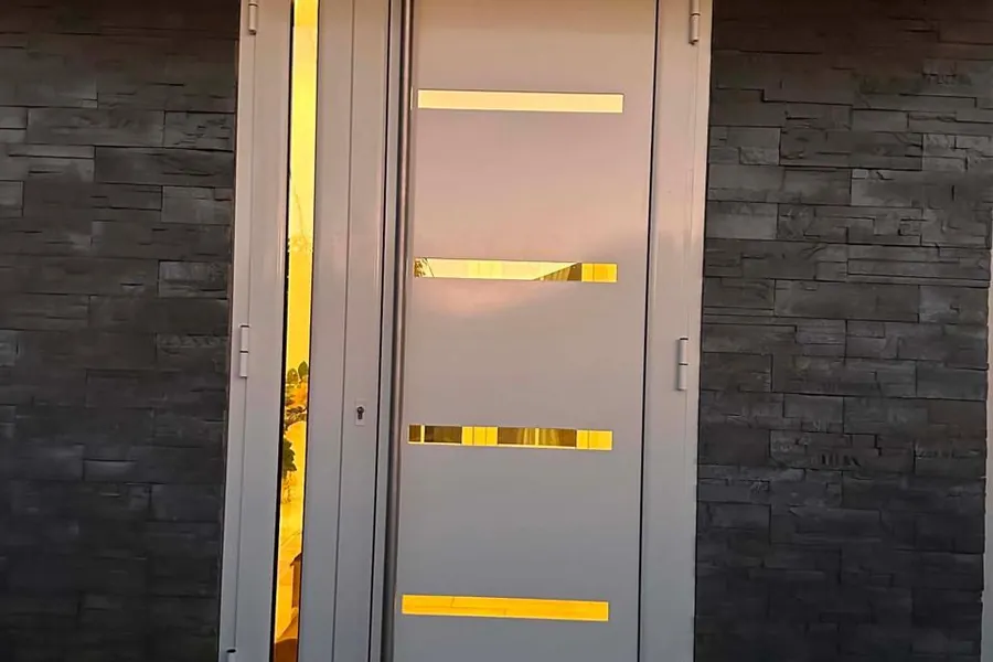 Porte d'entrée aluminium blanche à inserts vitrés et fixe latéral, sur un mur en parement de pierre