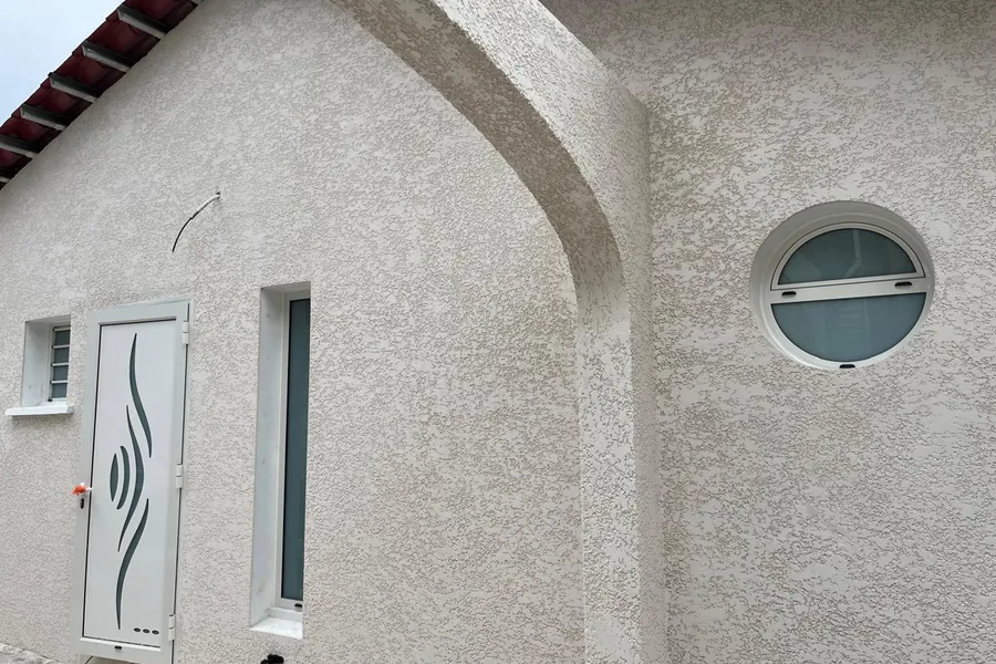Porte de service aluminium à motif décoratif et œil-de-bœuf rond ouvrant en demi-lune sur une façade crépie